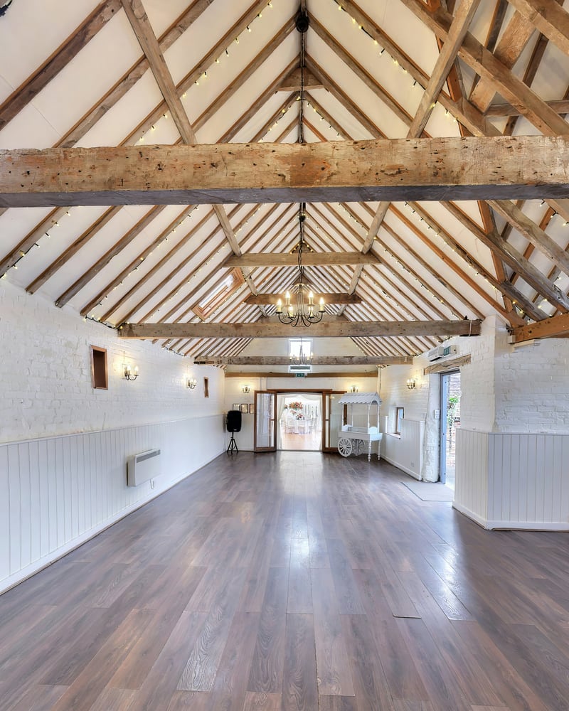 The length of the barn beneath its oak roof trusses, strung with fairy lights and a chandelier, over a polished timber floor