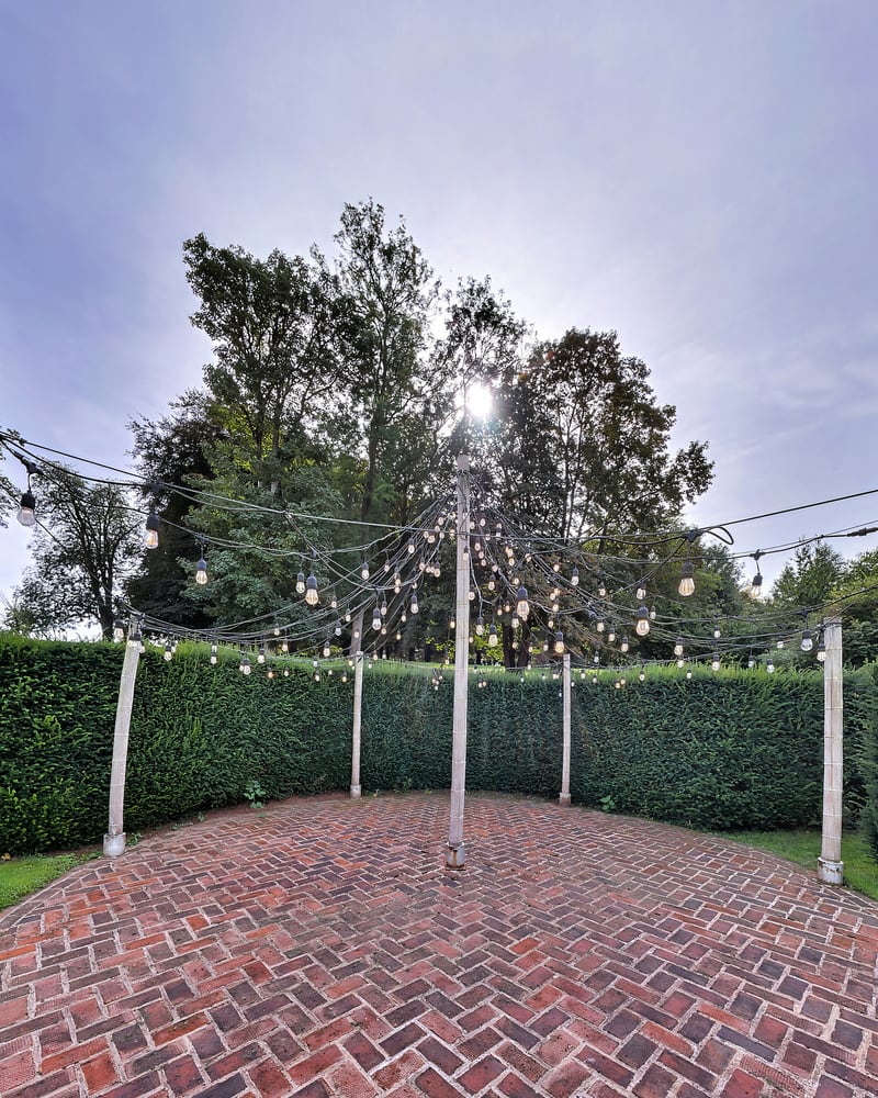 Festoon lights strung from a central maypole over a circle of herringbone brick, ringed by a yew hedge