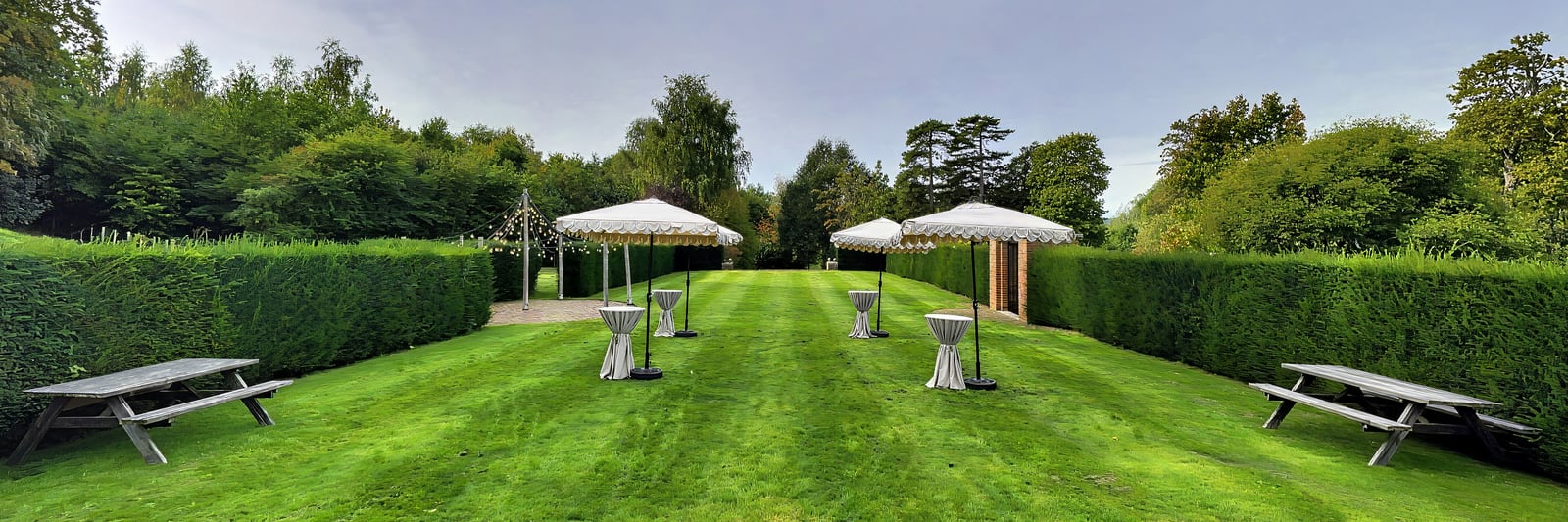 A long striped lawn between yew hedges, set with scalloped parasols and poseur tables for drinks