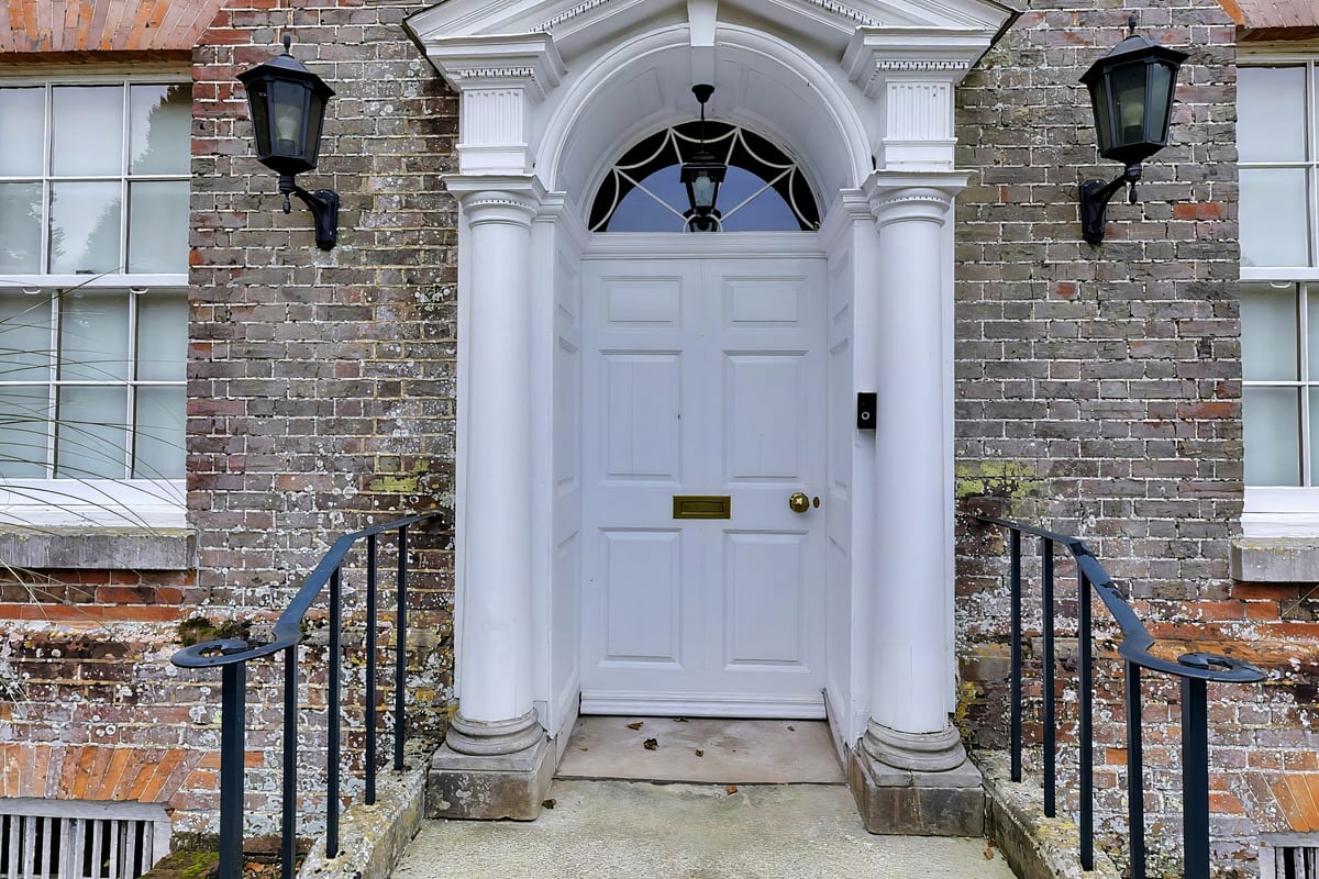 The manor's white panelled front door with a fanlight and pillared doorcase, flanked by lanterns and iron railings